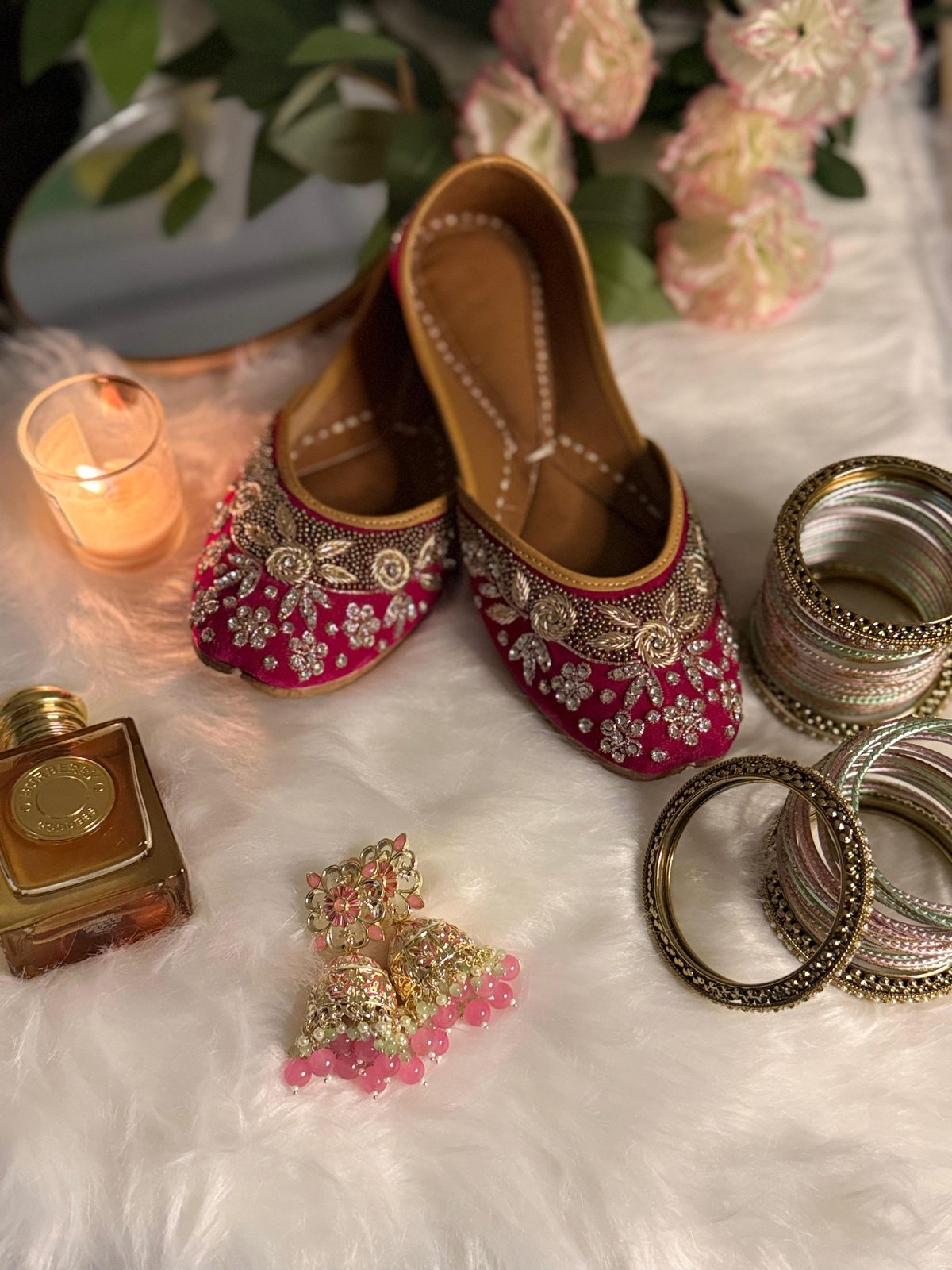 Magenta embroidered juttis with bangles, jhumkas, and perfume in candlelight
